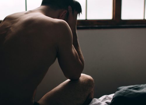 A stressed young man is sitting alone on the bed, putting his hands on his head | Avail Aesthetics in Cary, NC